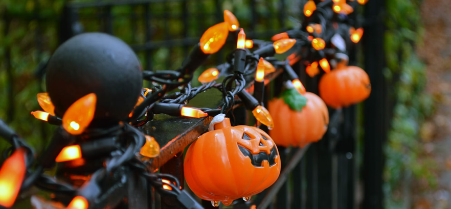 A black metal fence with orange lights and pumpkin decorations.